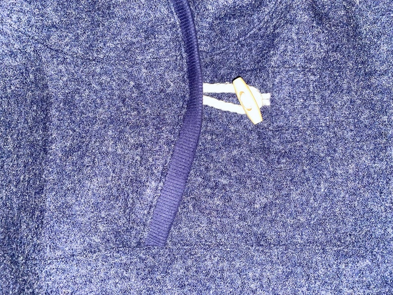 May include: A close-up of a blue sweater with a white toggle closure.