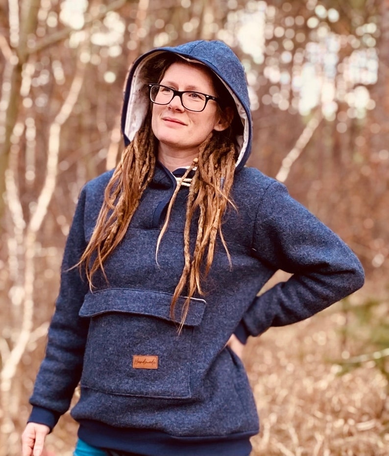 May include: A dark blue hooded sweatshirt with a large front pocket and a brown leather patch that says "Handmade". The sweatshirt has a white fleece lining around the hood.