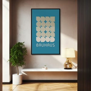 May include: A framed Bauhaus art print with a teal background and a geometric pattern of beige shapes. The word "BAUHAUS" is printed in white. The print hangs on a wall above a white shelf, with a small plant and a lamp.