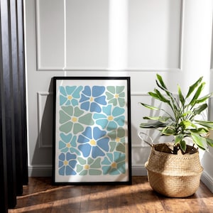 May include: A framed art print featuring a floral pattern in shades of blue and green with yellow centers. The artwork is displayed on a wooden floor, next to a woven basket with a green plant.