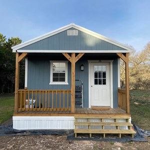 May include: A small, blue, wooden house with a white trim and a wooden porch. The house has a white door and a window on the left side. There are wooden steps leading up to the porch.