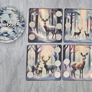 May include: Five square wooden tiles with a winter forest scene and white dots. Each tile features a different deer with a snowy background. The tiles are part of a game.