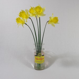 May include: A bouquet of yellow daffodils in a clear glass bottle with a yellow and red label that reads "Topo Chico Mineral Water".