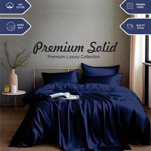 May include: A navy blue king-size bed sheet set with a satin finish. The set includes a flat sheet, fitted sheet, and two pillowcases. The sheet set is made of 100% cotton and is super soft. The image shows the sheet set on a bed with a white headboard and a wooden nightstand. The text "Premium Solid" and "Premium Luxury Collection" is displayed on the image.