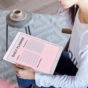 Può includere: Una persona sta usando un tablet con un'app di pianificatore giornaliero rosa e bianco. L'app ha sezioni per un elenco di cose da fare, un pianificatore del mattino e un pianificatore del pomeriggio. La persona indossa delle cuffie e siede su una sedia.