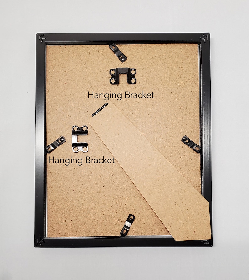 May include: Back of a black picture frame with a cardboard backing. The frame has metal hanging brackets and a cardboard stand. The text "Hanging Bracket" is printed on the cardboard.
