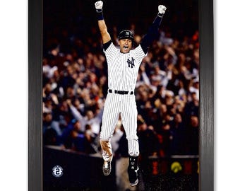 May include: A black and white baseball uniform with a New York Yankees logo. The player is jumping in the air with both arms raised in celebration. The player is in front of a blurred background of a cheering crowd.