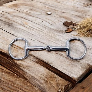 May include: A silver horse bit with a loose ring on each end. The bit is made of metal and has a smooth finish.