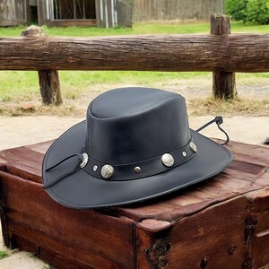 May include: A black leather cowboy hat with a silver concho band and a leather chin strap.