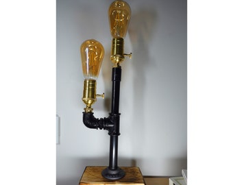May include: A black pipe table lamp with two Edison bulbs. The lamp has a wooden base and is on a table.