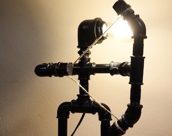 May include: A black metal lamp shaped like an archer with a bow and arrow. The lamp is made of industrial pipes and has a light bulb in the bow.