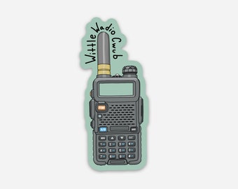 May include: A black and gray walkie talkie with a small antenna and a screen. The walkie talkie has a keypad with numbers and buttons. The text "Wittle Wadio Club" is written above the walkie talkie.