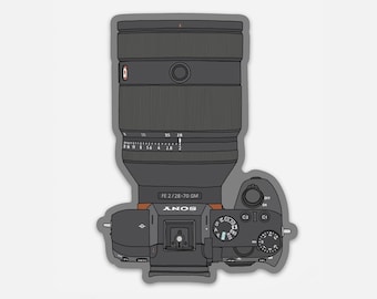 May include: Top-down view of a black Sony camera with a large lens. The lens is cylindrical with a red accent ring. The camera body has various dials and buttons. The text "FE 2/28-70 GM" and "SONY" are visible.