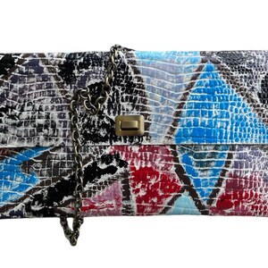 May include: A white leather clutch bag with a chain strap. The bag is decorated with a patchwork design of blue, red, and black paint.
