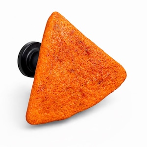 May include: A novelty shoe charm shaped like a triangular orange tortilla chip. The charm has a textured surface and is attached to a black base, designed to be inserted into the holes of a shoe.
