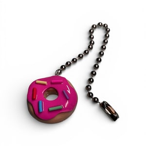 May include: A novelty ceiling fan pull chain featuring a pink glazed donut with colorful sprinkles. The donut charm is attached to a beaded chain with a decorative pull.