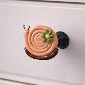 May include: A whimsical snail-shaped cabinet knob. The knob features a spiral shell in shades of peach and brown, with a green and pink flower accent. The snail has black antennae and is mounted on a black metal base. This decorative knob adds a playful touch to furniture.