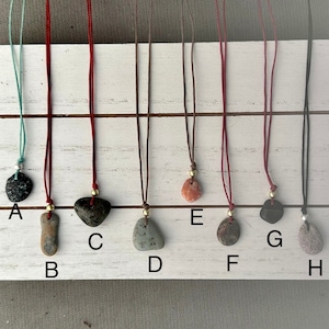 May include: Eight necklaces with different colored cords and unique stone pendants. The stones are various shapes and colors, including black, gray, brown, green, red, and pink.