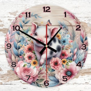 Könnte beinhalten: Eine runde Holzuhr mit einem Ferkel, das von rosa und weißen Blumen umgeben ist. Das Zifferblatt der Uhr hat schwarze Zahlen und Zeiger. Das Ferkel ist weiß mit schwarzen Flecken und hat eine rosa Nase.