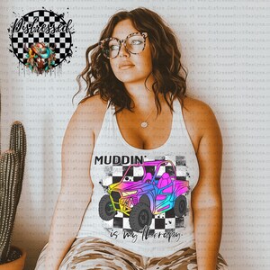 May include: A white tank top featuring a rainbow coloured graphic of an off-road vehicle. The graphic has a chequered background and the text "MUDDIN' is my therapy."