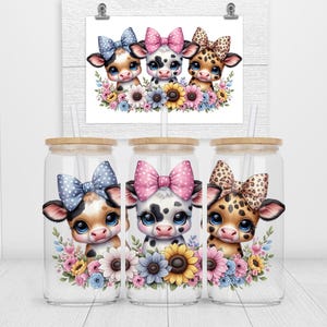 以下が含まれることがあります： 竹製の蓋とストローが付いたガラスタンブラー3個。それぞれにリボンと花のアクセントが付いた漫画の牛が描かれています。牛はそれぞれ異なる模様とリボンの色（青い水玉、ピンクの水玉、ヒョウ柄）をしています。