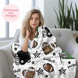 Può includere: Una coperta bianca a tema football, con palloni da football marroni, caschi neri e stelle a scacchi. La parola "football" è scritta in corsivo. La coperta ha accenti verdi e una bandiera a scacchi.