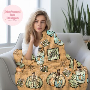 May include: A tan blanket with a fall theme, featuring pumpkins, coffee cups, and the word "Fall" in a repeating pattern. The blanket has a light blue bow and leaf design. The blanket is draped over a white chair.