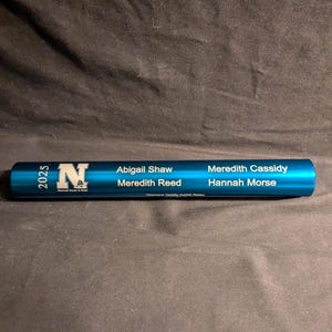 May include: A teal blue track and field relay baton. The baton has the text "2025" and a logo with the letter "N". The names Abigail Shaw, Meredith Reed, Meredith Cassidy, and Hannah Morse are printed on the baton.