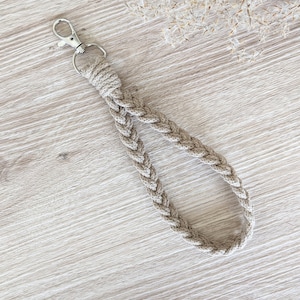 Könnte beinhalten: Ein geflochtener Schlüsselanhänger in Beige mit einem silbernen Metallverschluss.