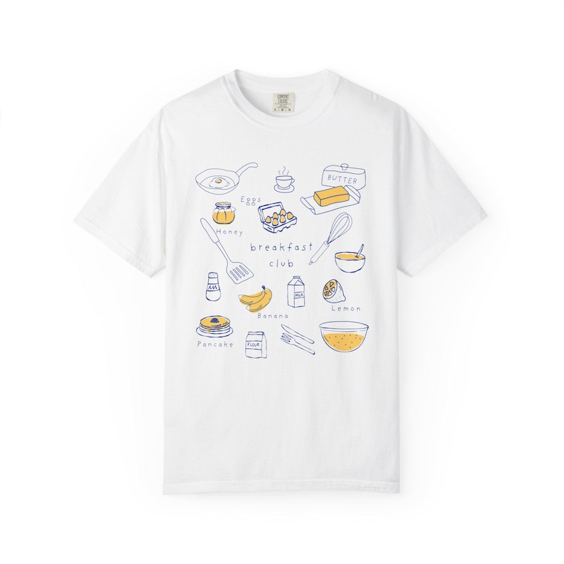 K&ouml;nnte beinhalten: Wei&szlig;es T-Shirt mit einer blauen Strichzeichnung von Fr&uuml;hst&uuml;ckszutaten, darunter eine Bratpfanne, Eier, Butter, Pfannkuchen und die Worte "breakfast club". Das Shirt hat einen Rundhalsausschnitt und kurze &Auml;rmel.