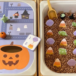 May include: A Halloween-themed sensory bin with two sections. One features a pumpkin, a road map, and Halloween figures. The other contains beans, scoops, and Halloween-themed cutouts. A fun, educational toy.