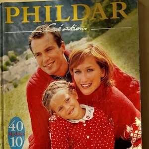 Könnte beinhalten: Ein Buchcover mit einer Familie, die rote Pullover mit weißen Schneeflockenmustern trägt. Der Buchtitel lautet "PHILDAR Creations" und der Text "40 modèles pour un hiver tout en couleur" befindet sich am unteren Rand des Covers.