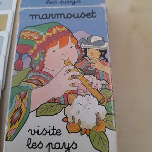 May include: A vintage card game box with a cartoon illustration. The box features a child playing a flute, wearing a colorful hat and clothing. The text "marmouset" and "visite les pays" are visible on the box.