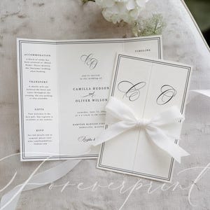 May include: A sophisticated wedding invitation set, comprising a tri-fold card and a smaller card secured with a white satin ribbon. The cards are white with black text and a minimalist design. A white flower and ribbon enhance the presentation.