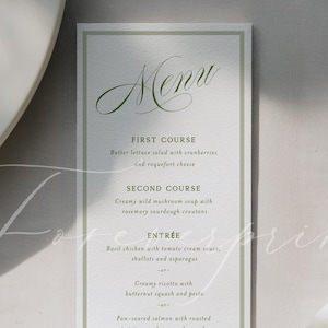 May include: A vertical menu card with a white background and a thin, light green border. The word "Menu" is written in elegant cursive at the top. The menu lists courses like "First Course" and "Second Course". A white ribbon is draped across the bottom.