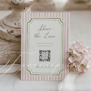 May include: A vertical sign with pink and white stripes, framed with green and a decorative border. The sign reads "Share the Love" and includes a QR code. A small bouquet of pink flowers and white ribbon are on the right.