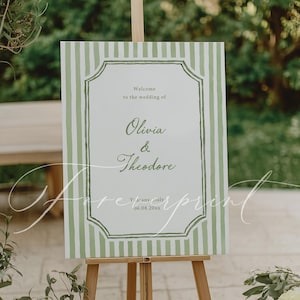 May include: A wedding welcome sign on a wooden easel. The sign features a white background with green vertical stripes and a decorative border. The text reads "Welcome to the wedding of Olivia & Theodore" and the date.
