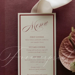 May include: A rectangular paper menu with a cream background and a dark red border. The text reads Menu, First Course, Butter lettuce salad with cranberries and roquefort cheese, Second Course, Creamy wild mushroom soup, Entrée, and Dessert.