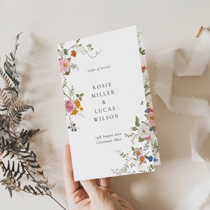 Könnte beinhalten: Ein weißes Hochzeits-Programm mit einem floralen Rand. Der Text lautet "Order of Service" und "Rosie Miller & Lucas Wilson" mit dem Datum "14. August 20xx" und dem Ort "Cleveland, Ohio".