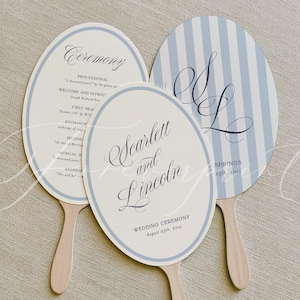 May include: Three oval-shaped hand fans with light blue and white stripes and borders. The fans feature printed text including "Ceremony," "Scarlett and Lincoln," and "Wedding Ceremony August 25th, 20xx," along with script initials "S & L" on wooden handles.