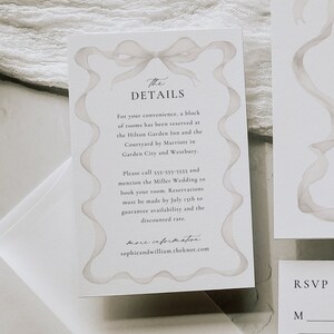 May include: A white wedding invitation card with a watercolor illustration of a bow. The text on the card reads "The Details" and includes information about hotel room reservations for the Miller Wedding. The card also includes the website "sophieandwilliam.theknot.com".