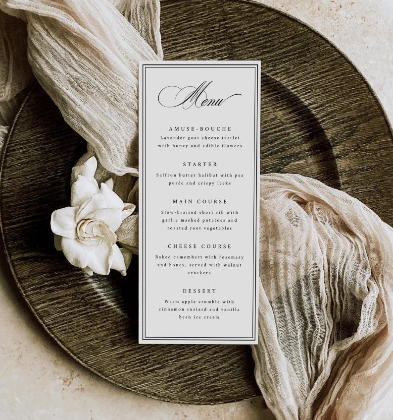 May include: A formal menu card with a black border, featuring elegant script and a list of courses. The menu is on a textured, dark plate, with a white flower and draped fabric. The menu includes Amuse-bouche, Starter, Main Course, Cheese Course, and Dessert.