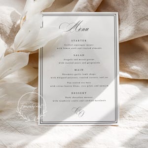 K&ouml;nnte beinhalten: Eine formelle Men&uuml;karte mit schwarzem Rand und eleganter Schrift. Das Men&uuml; listet eine Vorspeise, einen Salat, ein Hauptgericht und ein Dessert auf. Die Karte liegt auf einer cremefarbenen Oberfl&auml;che mit wei&szlig;en floralen Akzenten.