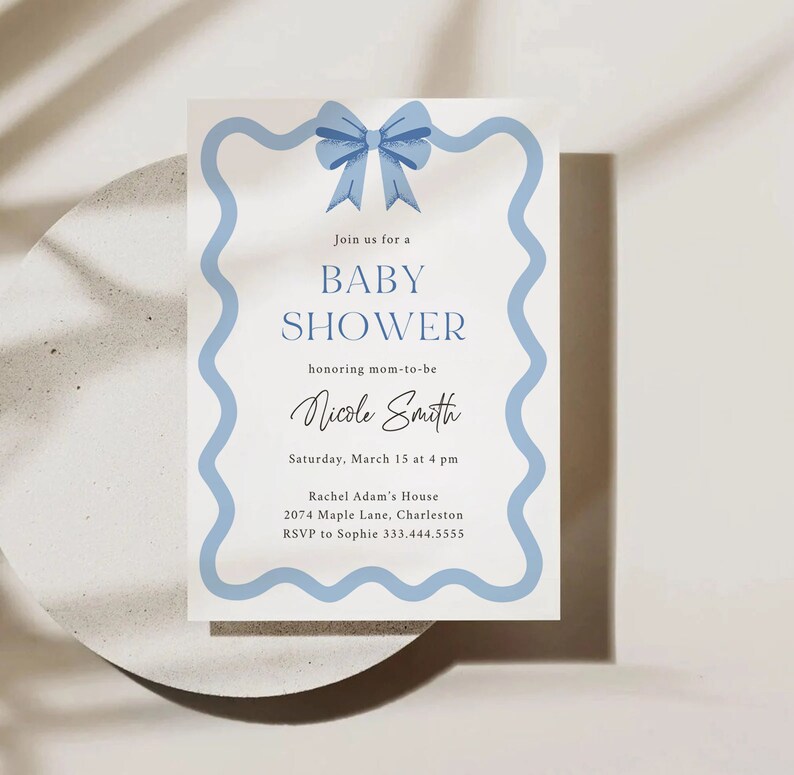 Peut inclure: Une invitation de f&ecirc;te pr&eacute;natale bleue et blanche avec un n&oelig;ud bleu en haut. L'invitation indique "Rejoignez-nous pour une f&ecirc;te pr&eacute;natale en l'honneur de la future maman Nicole Smith. Samedi 15 mars &agrave; 16h00. Maison de Rachel Adam, 2074 Maple Lane, Charleston. RSVP &agrave; Sophie 333.444.5555"