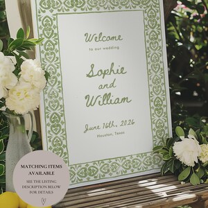 May include: A white welcome sign with a green border featuring a decorative pattern. The sign reads "Welcome to our wedding Sophie and William June 16th, 2026 Houston, Texas".