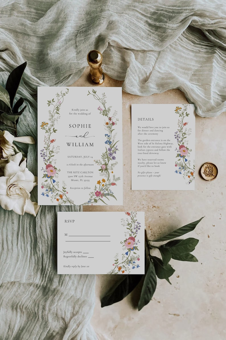 May include: A floral wedding invitation with a white background and a wreath of colorful flowers. The invitation includes the names Sophie and William, the date Saturday, July 14, and the time 1 o'clock in the afternoon. The invitation also includes the location, The Ritz Carlton, 1900 SW 19th Avenue, Miami, FL 33135. The invitation also includes a RSVP card with the text "Joyfully accepts" and "Regretfully declines".