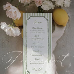 Op de afbeelding: Een menukaart met een groen-witte gestreepte rand, met een lijst met gerechten. Het menu bevat "Amuse-Bouche", "Voorgerecht", "Hoofdgerecht", "Kaasgang" en "Dessert". De kaart is versierd met bloemen en citroenen.