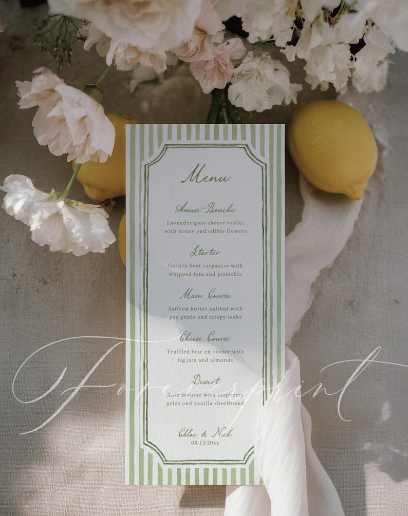 Op de afbeelding: Een menukaart met een groen-witte gestreepte rand, met een lijst met gerechten. Het menu bevat "Amuse-Bouche", "Voorgerecht", "Hoofdgerecht", "Kaasgang" en "Dessert". De kaart is versierd met bloemen en citroenen.