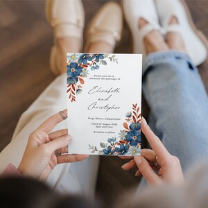 May include: A white wedding invitation with blue floral accents and text. The invitation reads "Elisabeth and Christopher" and includes event details. The design features watercolor-style flowers and foliage.