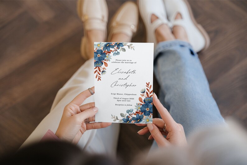 May include: A white wedding invitation with blue floral accents and text. The invitation reads "Elisabeth and Christopher" and includes event details. The design features watercolor-style flowers and foliage.